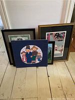 All five framed pieces grouped on floor against wall, showing different art styles and frames