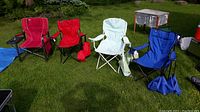 Four folding camping chairs in various colors lined up outside on grass with some carrying bags shown
