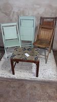 Front view of two wooden folding chairs and one folding stool with tribal patterned cushion on a rug, showing their overall structure and worn condition.