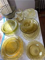 Top view of yellow Depression glass assortment on table, showing multiple plates, bowls, covered dishes, and serving pieces with intricate pressed patterns.