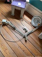 Full view of the adjustable desk lamp with clamp and cord on wooden floor near a small stool.