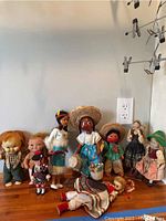 Photo showing a collection of nine dolls of various cultural backgrounds including Native American, Ukrainian, Scottish, and Mexican traditional outfits.