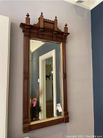 Full view of the Eastlake style wood framed mirror mounted on wall with intricate carved details and finials, reflective glass.