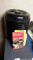 Photo of black Ronco food dehydrator stacked unit with instruction and recipe book placed in front