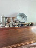 Wide view of metalware including pewter pot, copper cups, silver plated pitcher, and assorted bowls showing variety and condition.