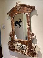 Front view of the framed wall mirror showing the distressed wooden frame with white paint residue and decorative metal grille.
