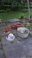 Lot overview showing large resin planter alongside smaller terracotta planters and galvanized metal tub on stone patio outdoors.