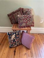 Photo showing five assorted throw pillows in various tapestry and fabric patterns on and around a wooden side table.