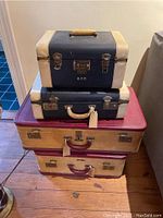 Four vintage hard-sided suitcases stacked, showing size and color differences