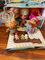 Five vintage troll dolls displayed with colorful cardboard box in background