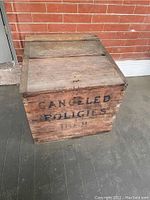 Front and top view of a vintage wooden crate with a hinged lid and 'CANCELED POLICIES' stenciled on the side.