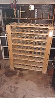 Front view of the wooden wine rack showing six tiers for wine bottle storage in a basement setting.