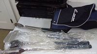 Four BBQ tools in plastic wrap - spatula, fork, brush, and gripper with black handles lying on floor next to golf bag carrier