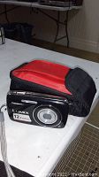 Panasonic Lumix black compact camera with 12.1MP label on front next to lens. Camera case next to camera, black with red interior.