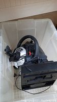 Logitech car racing steering wheel with pedal base unit inside a large plastic container.