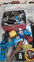 Photo showing assorted hand tools including scissors, wrenches, screwdrivers, a tape measure, and a level inside and outside a holiday-themed storage box.