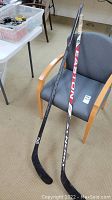 Two hockey sticks, one Sherwood and one Easton, resting on a chair showing overall length and condition.