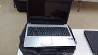 Hewlett Packard laptop model G61423CA open on black carrying bag. Screen is off, silver body and fully visible keyboard.
