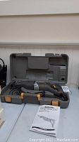 View of the reciprocating saw in its open hard plastic case with power cord wrapped and instruction manual in front