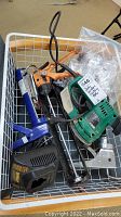 Top view of items in basket showing Craftsman circular palm sander, Dewalt charger, and three caulking tools.
