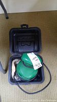 Green TurtleWax palm sander inside black molded plastic carrying case with latch.