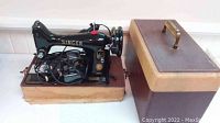 Front and side view of Singer sewing machine in wood box with lid beside it, foot pedal and cords visible.