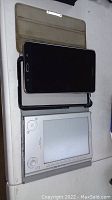 Samsung tablet and Sony portable reader system placed side by side on white table, tablet in brown cover.