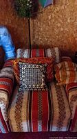 Photo of large patterned upholstered armchair with three different toss pillows and striped blanket placed on it in a basement setting.