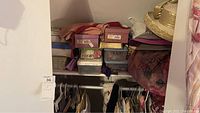 Photo showing closet with multiple shoeboxes stacked on shelves, clothing hanging on rods below, and hats placed on upper shelves.