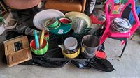 Overview of lot including cutting board set, watermelon-themed bowls and decor, metal cup caddy, flatware, plastic platters, oven trim rings, and two pink kid chairs with worn condition.