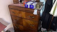 Front and partial side view of a wooden dresser showing three drawers with metal handles and geometric wood grain pattern on drawer fronts. Top surface has various items placed on it, which are not included.
