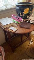 Wooden drop leaf table seen from an angle with the right leaf folded down and the left leaf partially visible. Several items rest on the table surface which has visible marks and crazing.