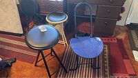 Photo showing four lightweight folding chairs: one blue folding chair with backrest and three round stool-style folding chairs in black and white