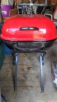 Front view of the Aussie charcoal grill with bright red lid and black stand.