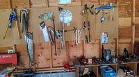 Wide view of pegboard with various hanging hand tools including saws, hammers, clamps, and other tools, plus several items on shelves below.