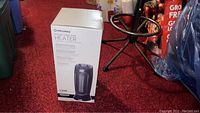 Pelonis heater in original box standing on red carpet, showing product image and text