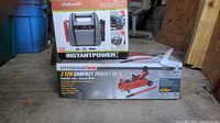 Shot showing the boxed Pittsburgh 2 ton compact trolley jack and Schumacher jump starter box stacked in garage.