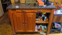 Front view of kitchen island showing stone top, drawers, cabinet doors, and open shelving with kitchen items inside.