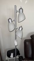 Lamp shown from front side with all three white frosted glass shades visible on a silver metal pole.