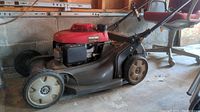 Full side view of the gray and red Honda lawn mower showing wheels, handle, and deck.