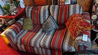 Front view of a patterned upholstered loveseat with colorful geometric and floral fabric, two accent pillows placed on it.