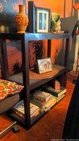 Black plastic shelving unit with three shelves shown with various decorative items on and around it for context.