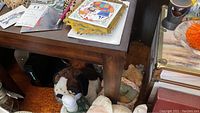 Close-up photo of dark brown wooden side table with stuffed animals and other items underneath, showing need for cleaning