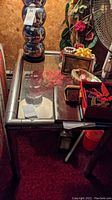 Photo showing one side table with metal frame and glass top, with decorative items on top
