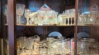 Cabinet with multiple clear glass stemware on upper and lower shelves including goblets, wine glasses, and cocktail glasses with mirror display panel behind.