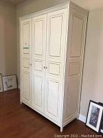 Front view of the distressed armoire showing the three paneled doors and cream finish.