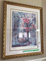 Framed print hanging on a wall showing a floral still life scene with a window background, signed by Marc Chagall