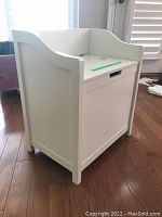 Front and side angled view of white wooden storage bench showing hinged seat with handle cut-out.