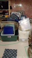 Photo of stacked plastic storage bins with lids in various colors and clear and white laundry baskets behind them.