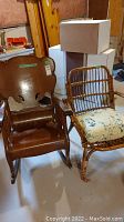 Photo showing two chairs side by side, one wooden vintage rocking chair with carved back and one rattan chair with a floral cushion.